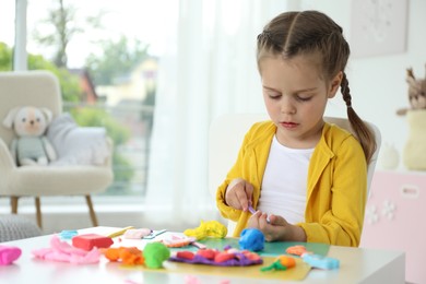 Little girl sculpting with play dough at table in kindergarten