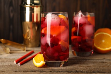 Photo of Tasty cranberry cocktail with ice cubes and orange in glasses on wooden table
