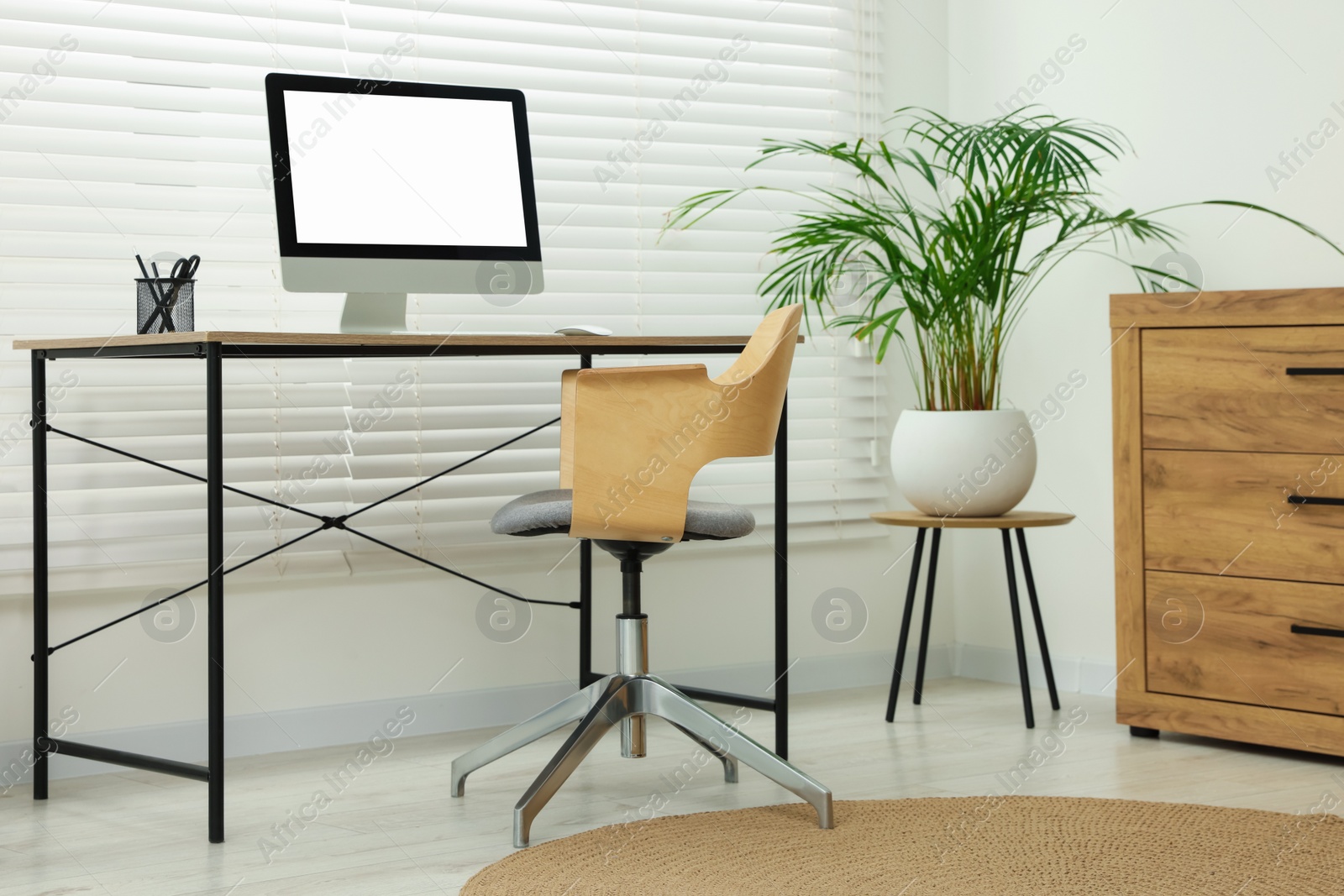 Photo of Stylish office interior with comfortable chair, desk, computer and houseplant