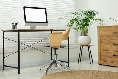 Stylish office interior with comfortable chair, desk, computer and houseplant