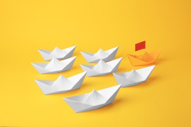 Photo of Group of paper boats following yellow one on color background. Leadership concept