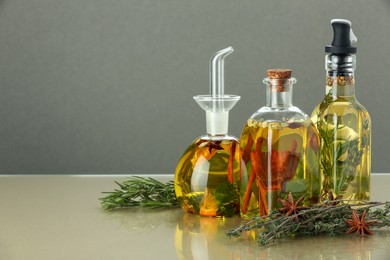 Photo of Cooking oil with different spices and herbs in bottles on beige table. Space for text