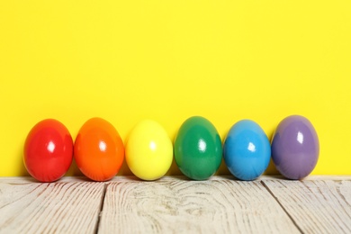 Easter eggs on white wooden table against yellow background, space for text