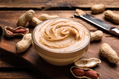 Photo of Yummy peanut butter in glass bowl on wooden table, closeup