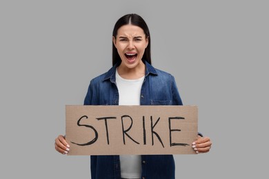 Angry woman holding cardboard banner with word Strike on grey background