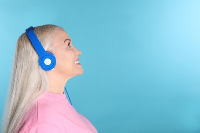 Photo of Mature woman enjoying music in headphones on color background. Space for text