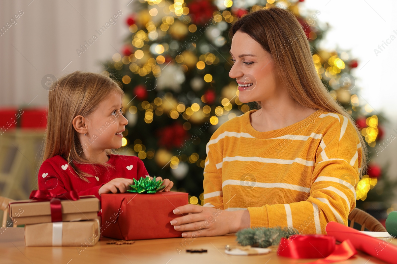 Photo of Christmas presents wrapping. Mother and her little daughter decorating gift box with bow at home