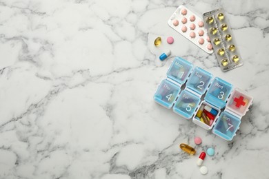Photo of Plastic box and different pills on white marble table, flat lay. Space for text