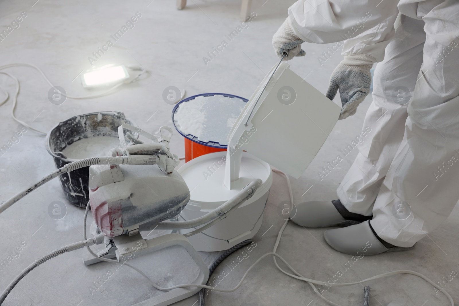 Photo of Decorator pouring paint in bucket on white floor, closeup