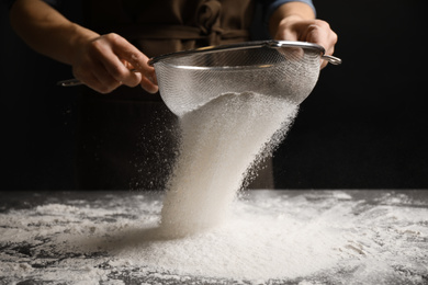 Photo of Woman sifting flour at grey table, closeup. Making pasta