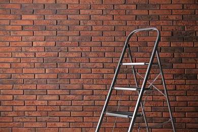 Photo of Modern metal stepladder against brick background. Space for text