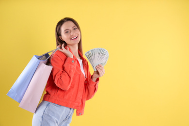 Photo of Young woman with money and shopping bags on yellow background. Space for text