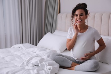 Photo of Pregnant young African-American woman sitting on bed at home