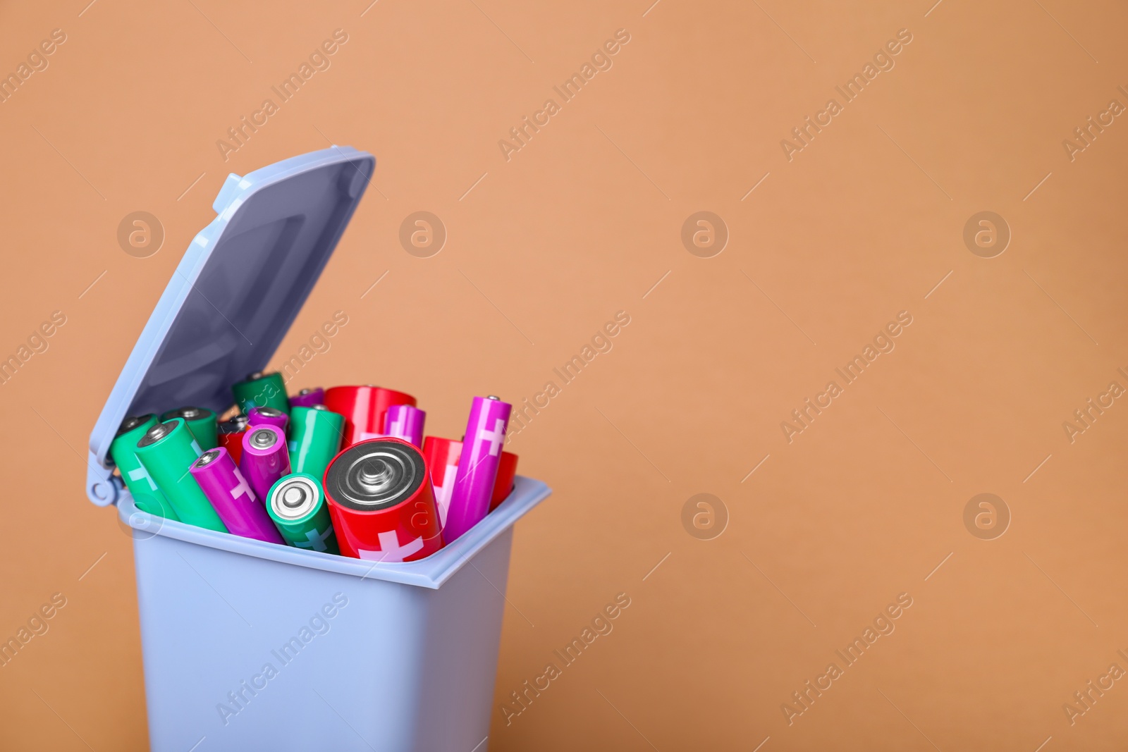 Photo of Many used batteries in recycling bin on coral background. Space for text