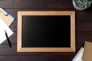 Photo of Clean small chalkboard, plant and stationery on wooden table, flat lay