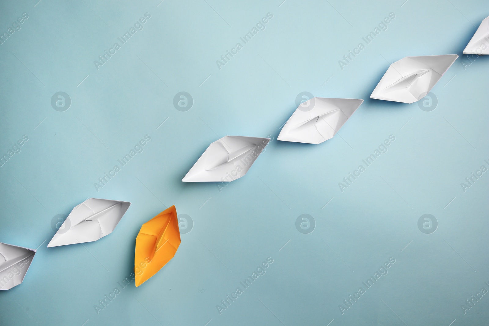 Photo of Yellow paper boat floating away from others on light background, flat lay with space for text. Uniqueness concept