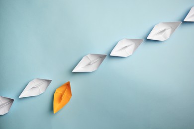 Photo of Yellow paper boat floating away from others on light background, flat lay with space for text. Uniqueness concept