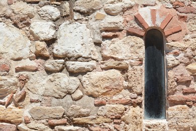 Old beige stone wall with arch window as background, closeup