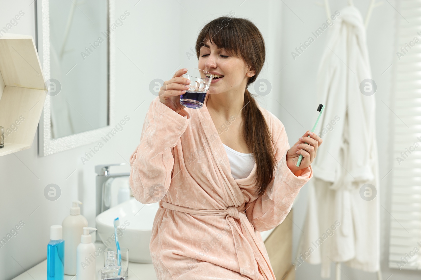 Photo of Young woman using mouthwash in bathroom. Oral hygiene