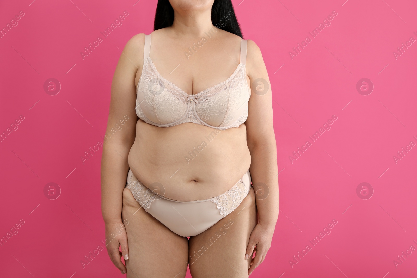 Photo of Overweight woman in beige underwear on pink background, closeup. Plus-size model