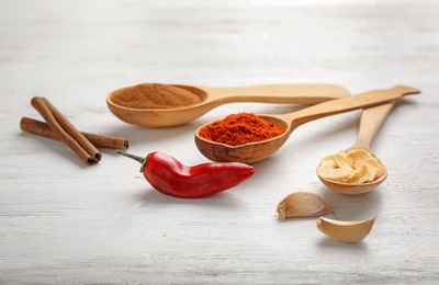 Photo of Different aromatic spices in wooden spoons on table, closeup