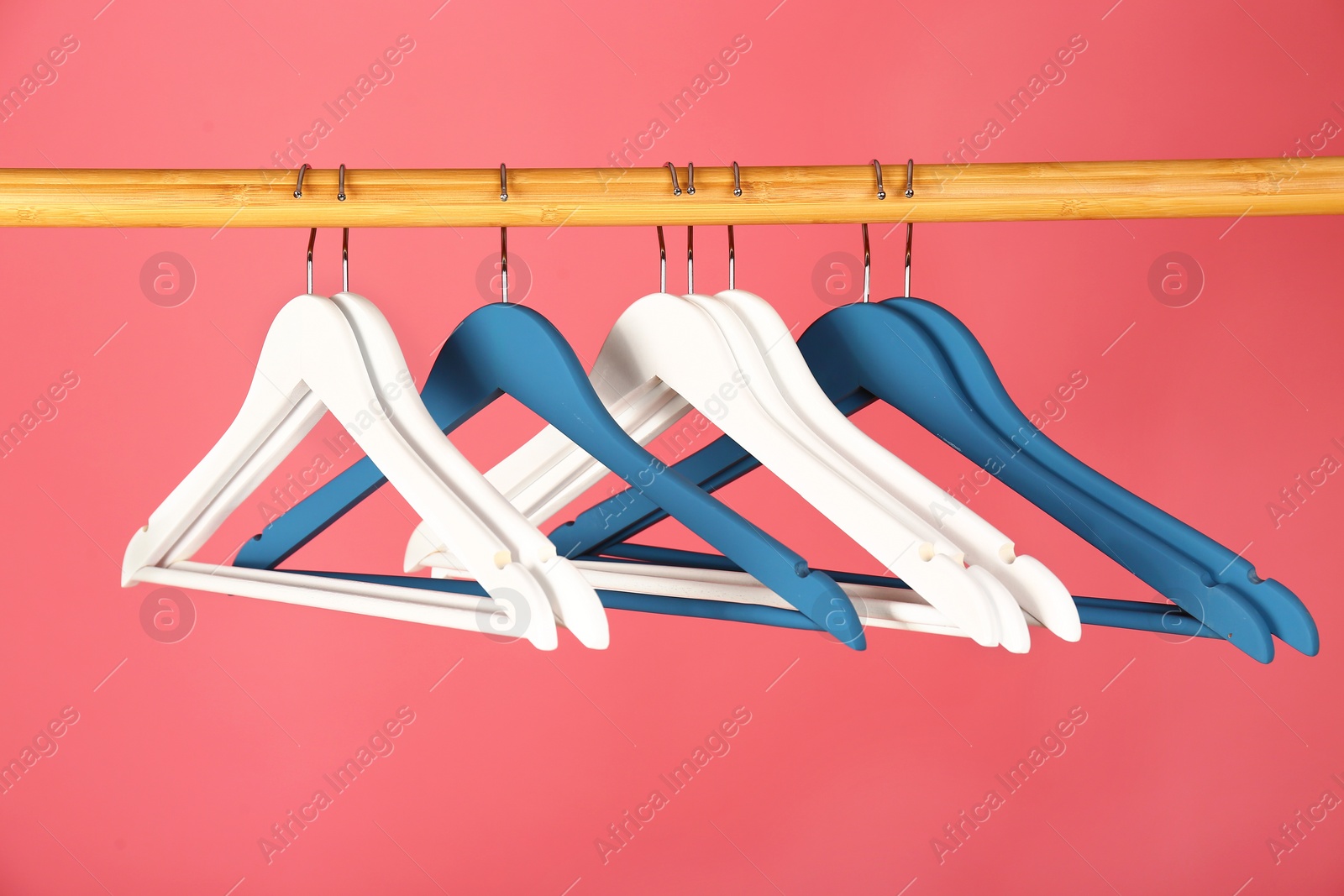 Photo of Empty clothes hangers on wooden rail against color background