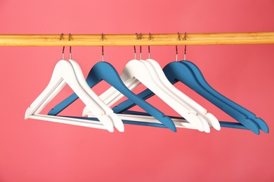 Empty clothes hangers on wooden rail against color background