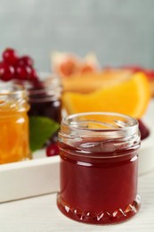 Photo of Open glass jar of sweet jam on white wooden table, closeup. Space for text