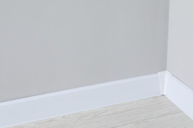 White plinth with connector on laminated floor near wall indoors, closeup