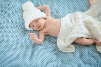 Photo of Adorable newborn baby in warm hat lying on bed, top view