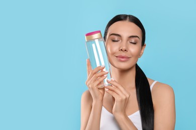 Photo of Young woman with bottle of micellar water on light blue background, space for text