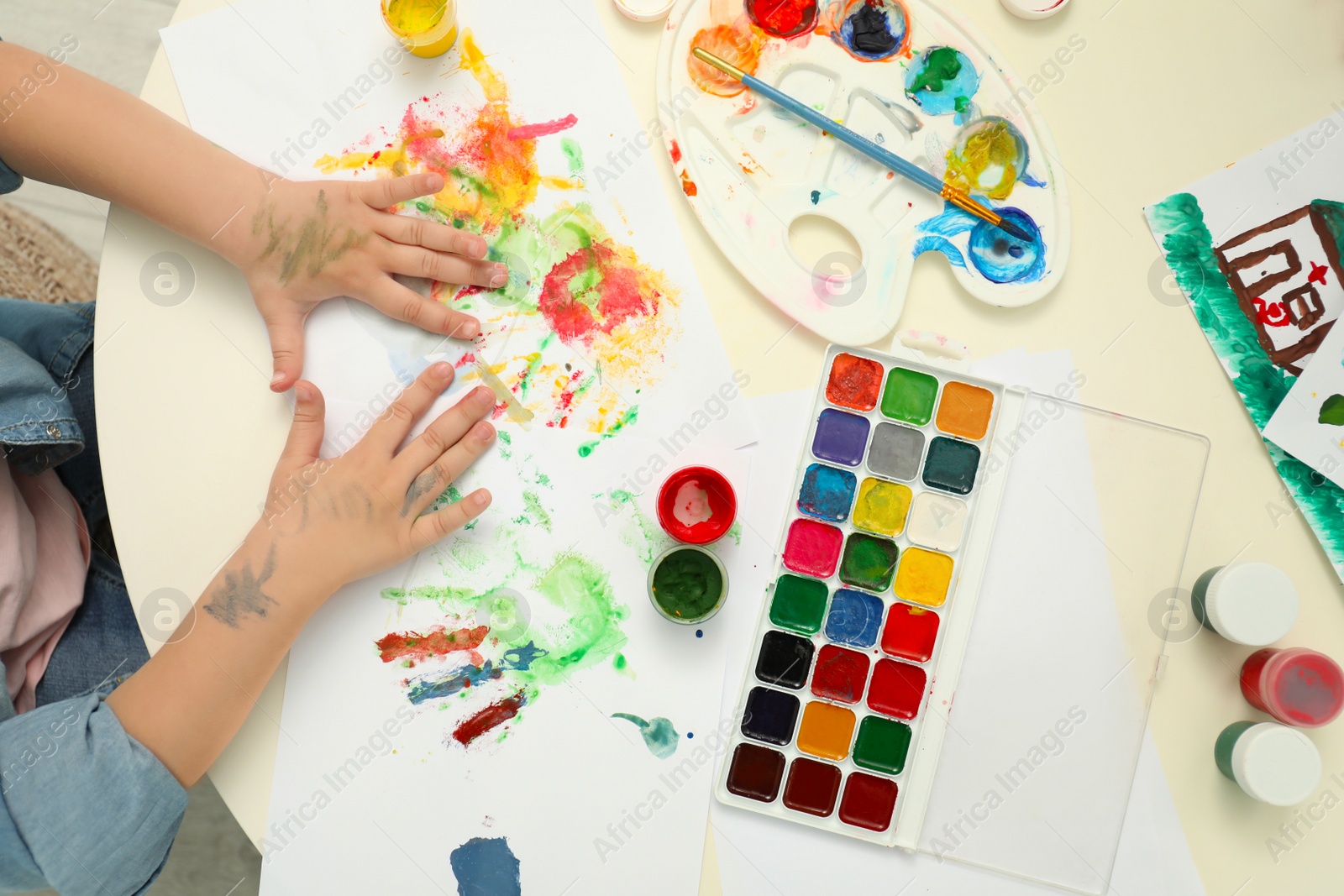 Photo of Little child painting with palms at table, top view