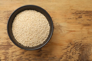 Photo of Dry quinoa seeds in bowl on wooden table, top view. Space for text