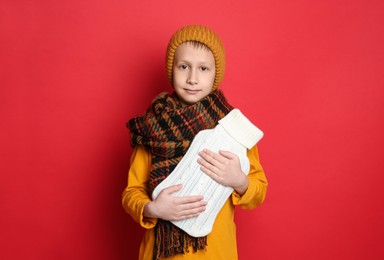 Photo of Ill boy with hot water bottle suffering from cold on red background