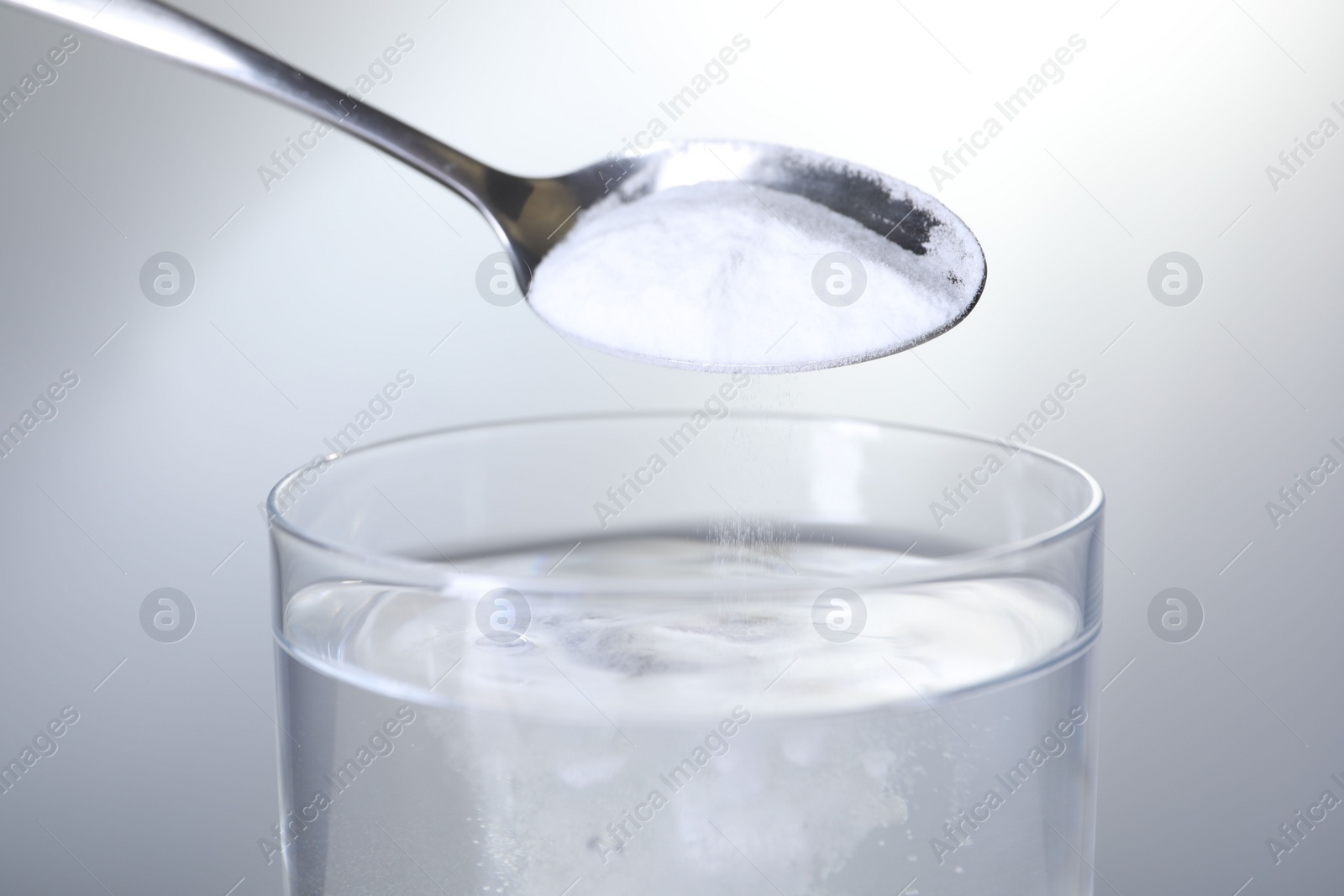 Photo of Adding baking soda into glass of water on light grey background, closeup