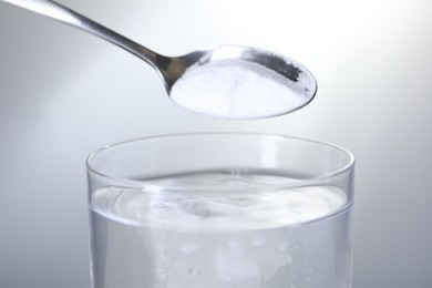 Adding baking soda into glass of water on light grey background, closeup