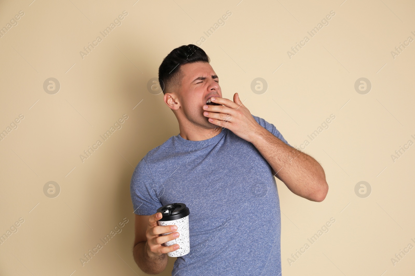 Photo of Tired man with mug of drink yawning on beige background