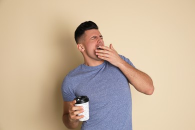 Tired man with mug of drink yawning on beige background