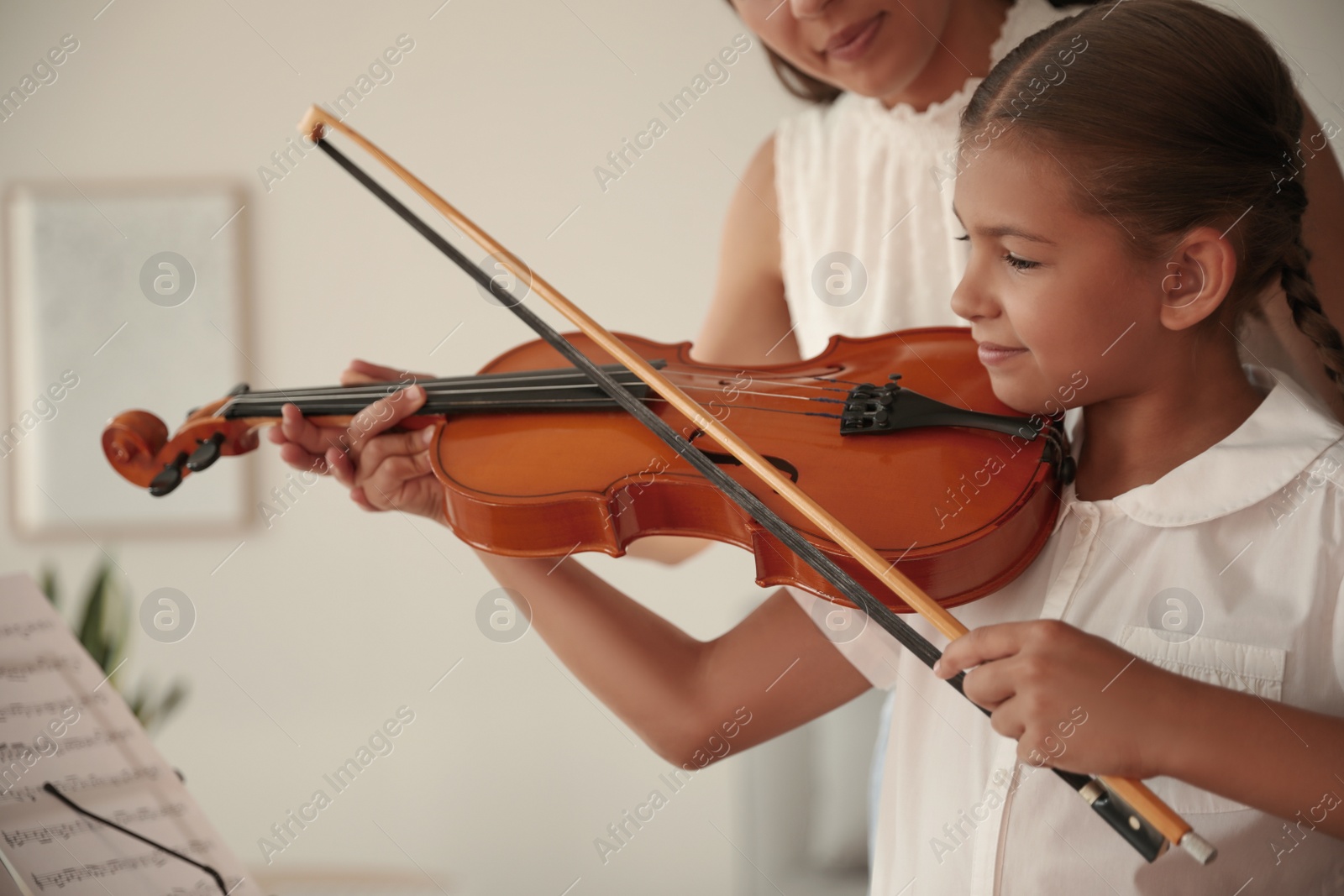 Photo of Young woman teaching little girl to play violin indoors