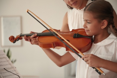 Young woman teaching little girl to play violin indoors