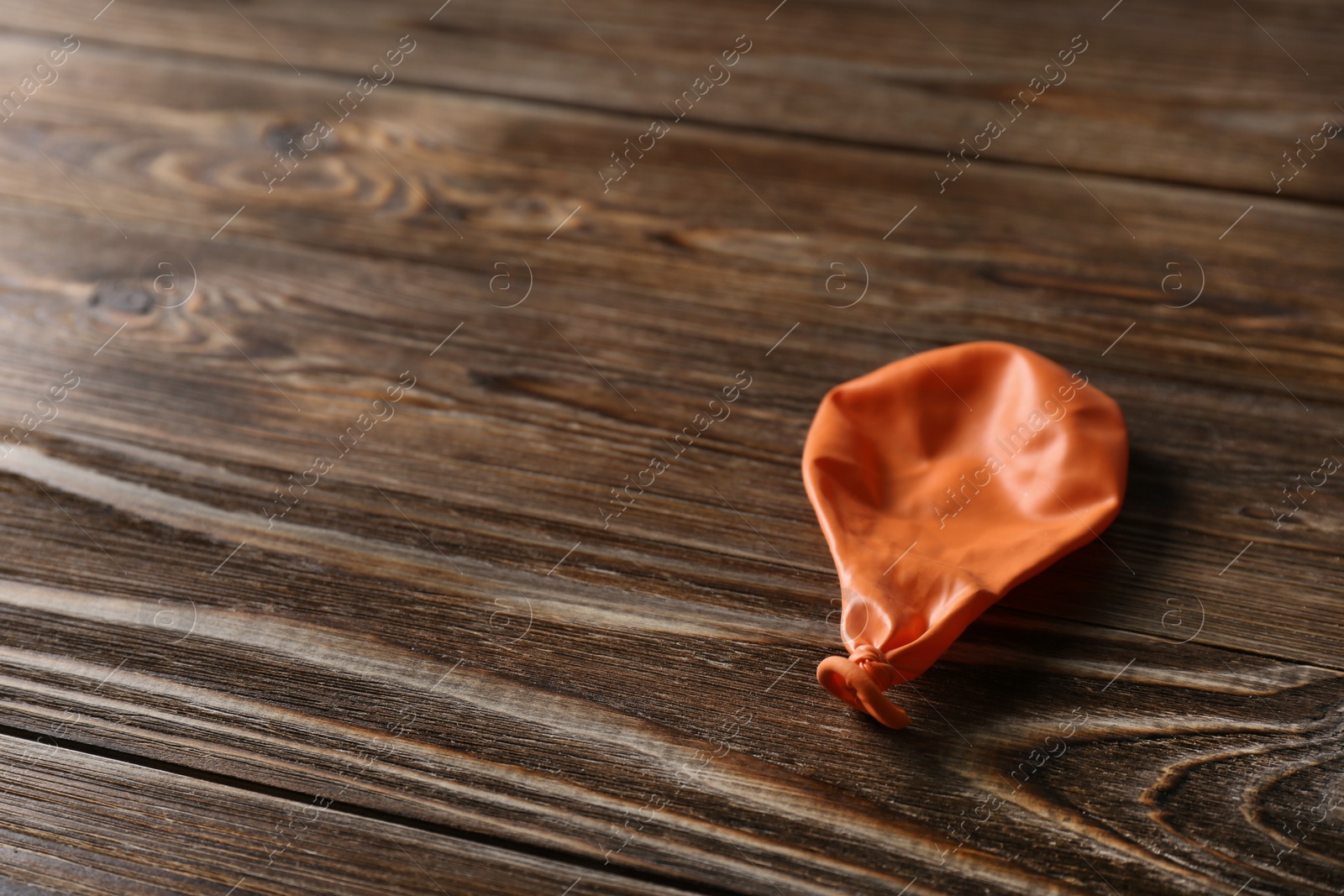 Photo of Orange deflated balloon on wooden background, space for text