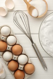 Bowl with whipped cream, whisk and ingredients on white wooden table, flat lay