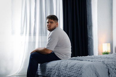 Photo of Depressed overweight man on bed at home