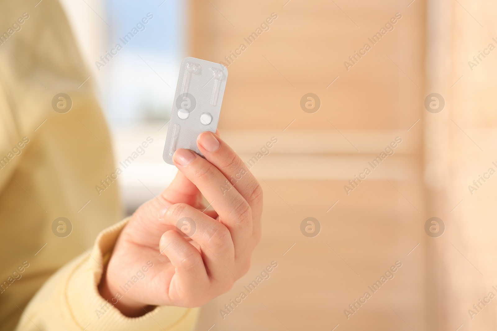 Photo of Woman holding blister of emergency contraception pills against blurred background, closeup. Space for text