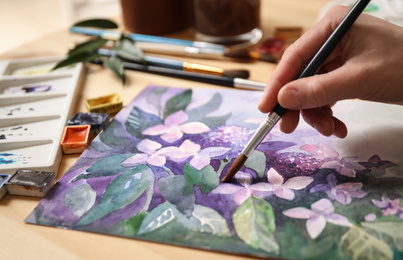Photo of Woman painting flowers with watercolor at table, closeup