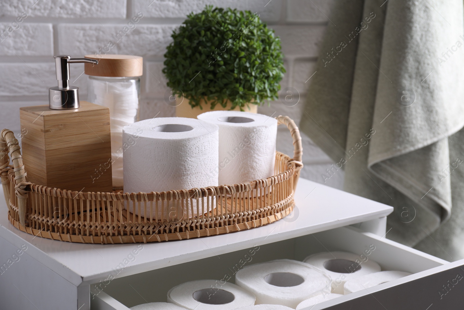 Photo of Toilet paper rolls, floral decor, dispenser and cotton pads on chest of drawers indoors