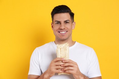 Man with delicious shawarma on yellow background