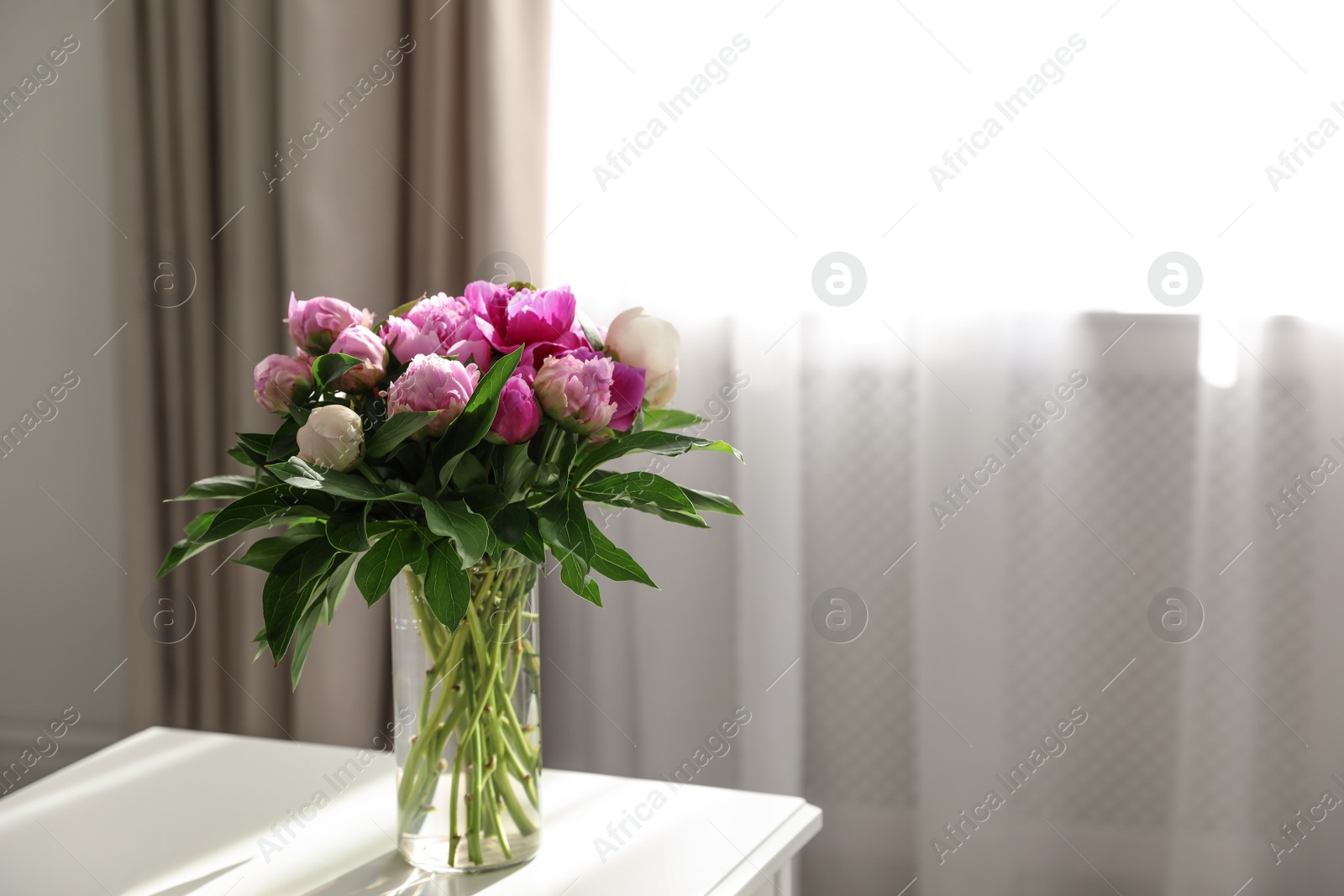 Photo of Vase with bouquet of beautiful peonies on table in room, space for text