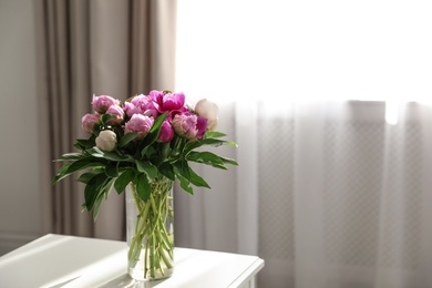 Photo of Vase with bouquet of beautiful peonies on table in room, space for text