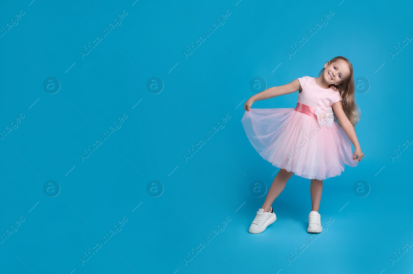 Photo of Cute little girl in beautiful dress dancing on light blue background. Space for text